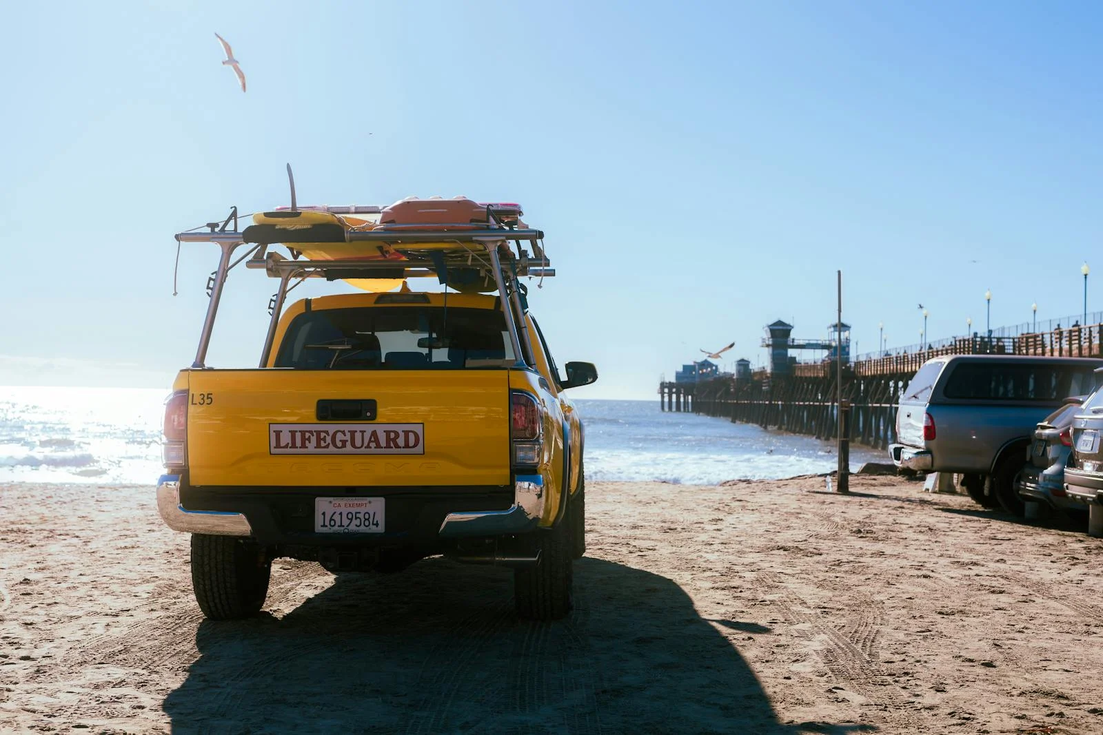 A yellow truck with surfboards on the back parked on the beach